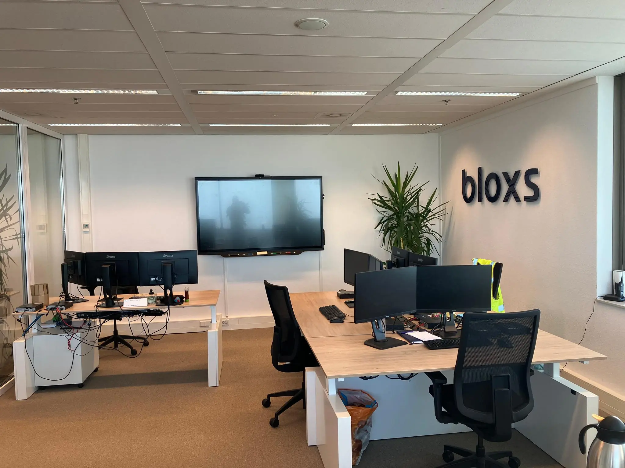 Moderne kantoorruimte aan de Vliegend Hertlaan met meerdere bureaus, beeldschermen en het logo van bloxs op de muur.